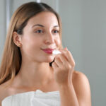 Young woman applying lip balm in front of the mirror indoor