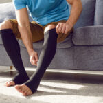 Man putting on medical compression stockings on legs for the prevention of varicose veins.