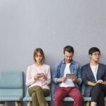 People, employment, recruitment, technology concept. Three unemployed people sit in queue, wait for job interview, use modern gadgets, prepare answers on tricky questions from boss or employer