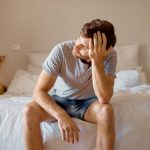 Depression, mental health and sad man in stress feeling bad, upset and depressed alone in his home, house or hotel suite. Wake up, morning and frustrated, unhappy male in bedroom tired with anxiety