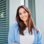 Happy caucasian young student female looking at camera enjoying with a perfect white teeth. Portrait of a joyful and adorable teenage brunette woman posing for a college promotion with crossed arms